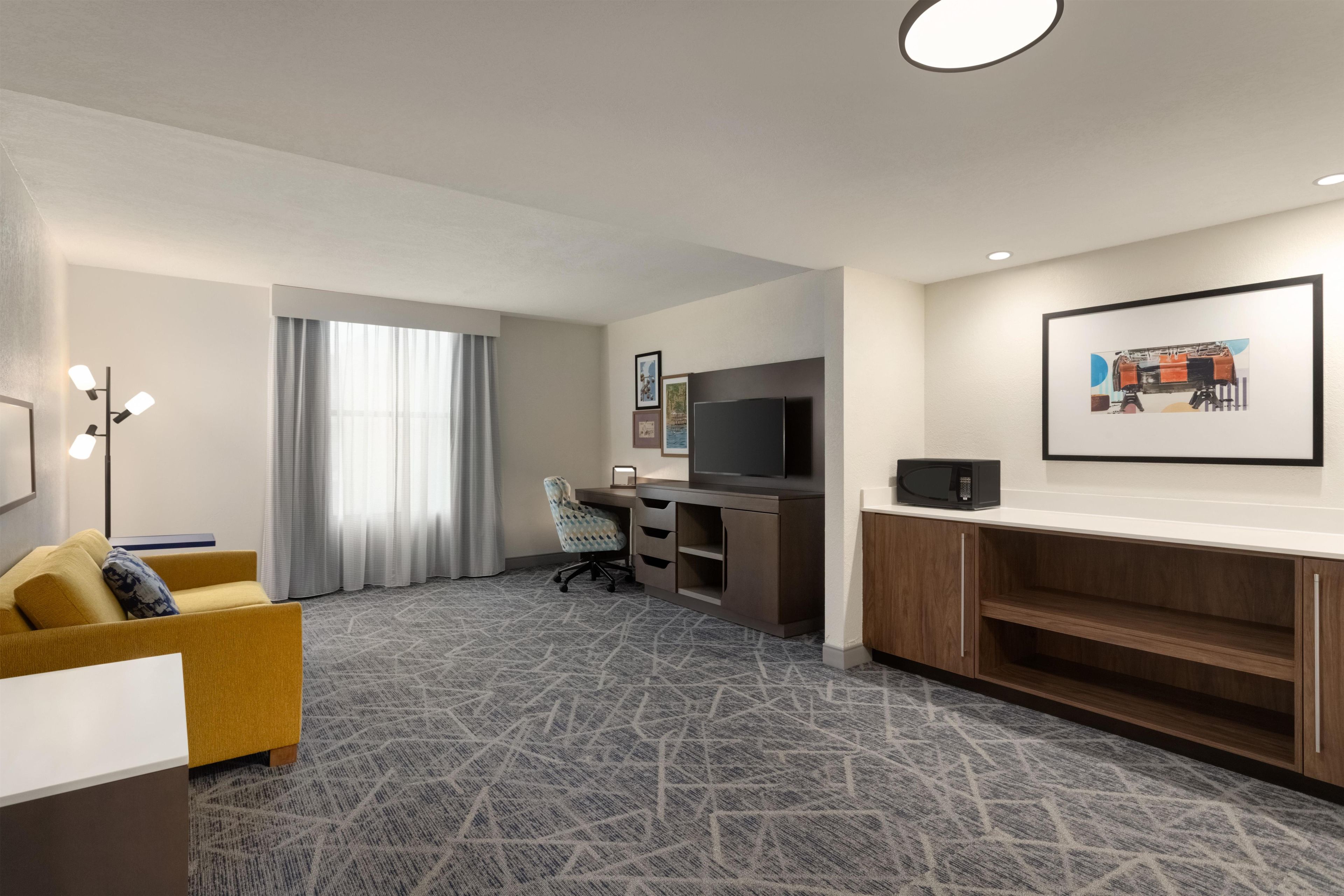 Une chambre d’hôtel équipée d’un canapé, d’un bureau avec un ordinateur, d’une télévision et d’un four à micro-ondes.
