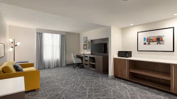 Une chambre d’hôtel équipée d’un canapé, d’un bureau avec un ordinateur, d’une télévision et d’un four à micro-ondes.