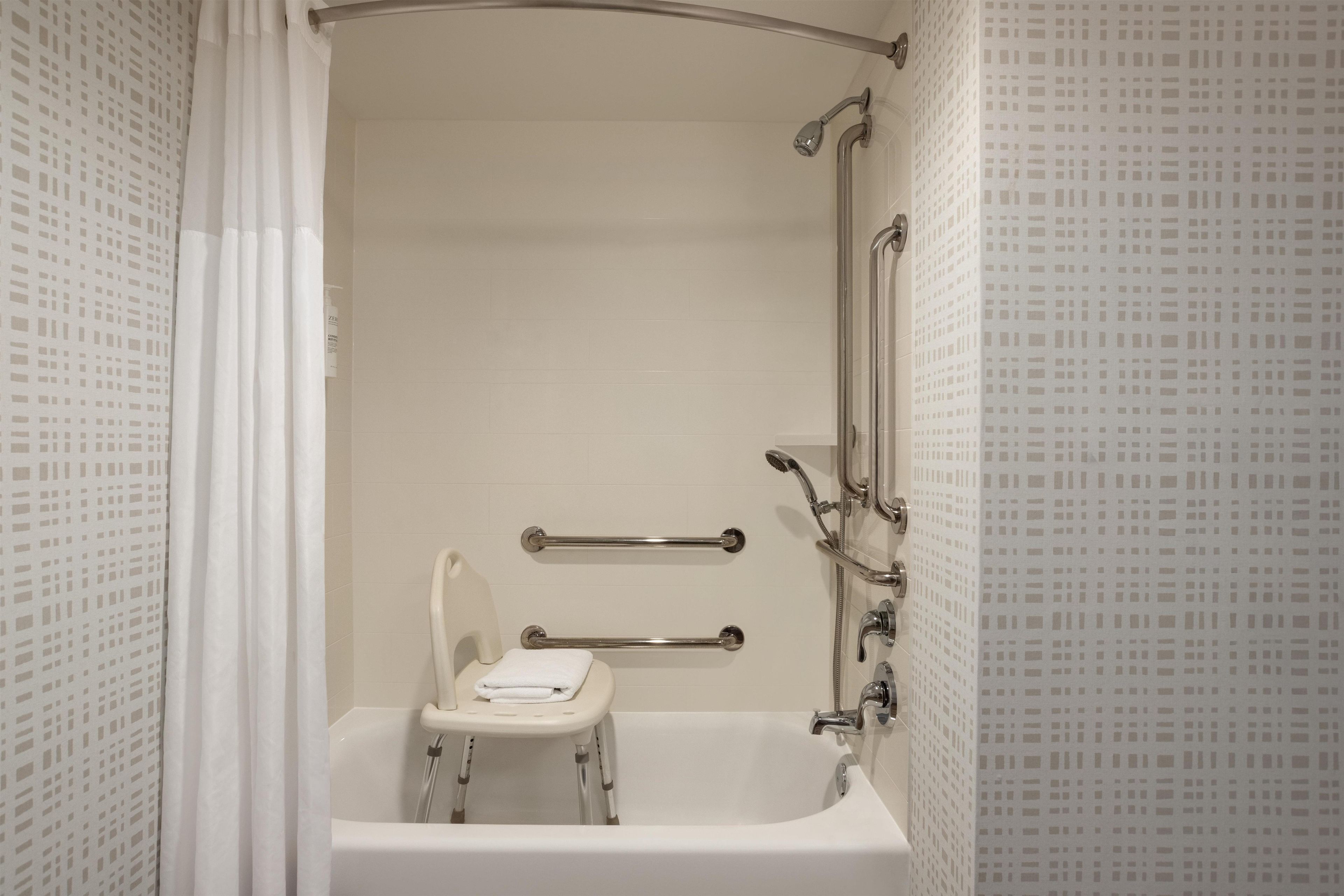 Un baño con bañera, ducha e inodoro. Cuenta con barras de apoyo para mayor seguridad.