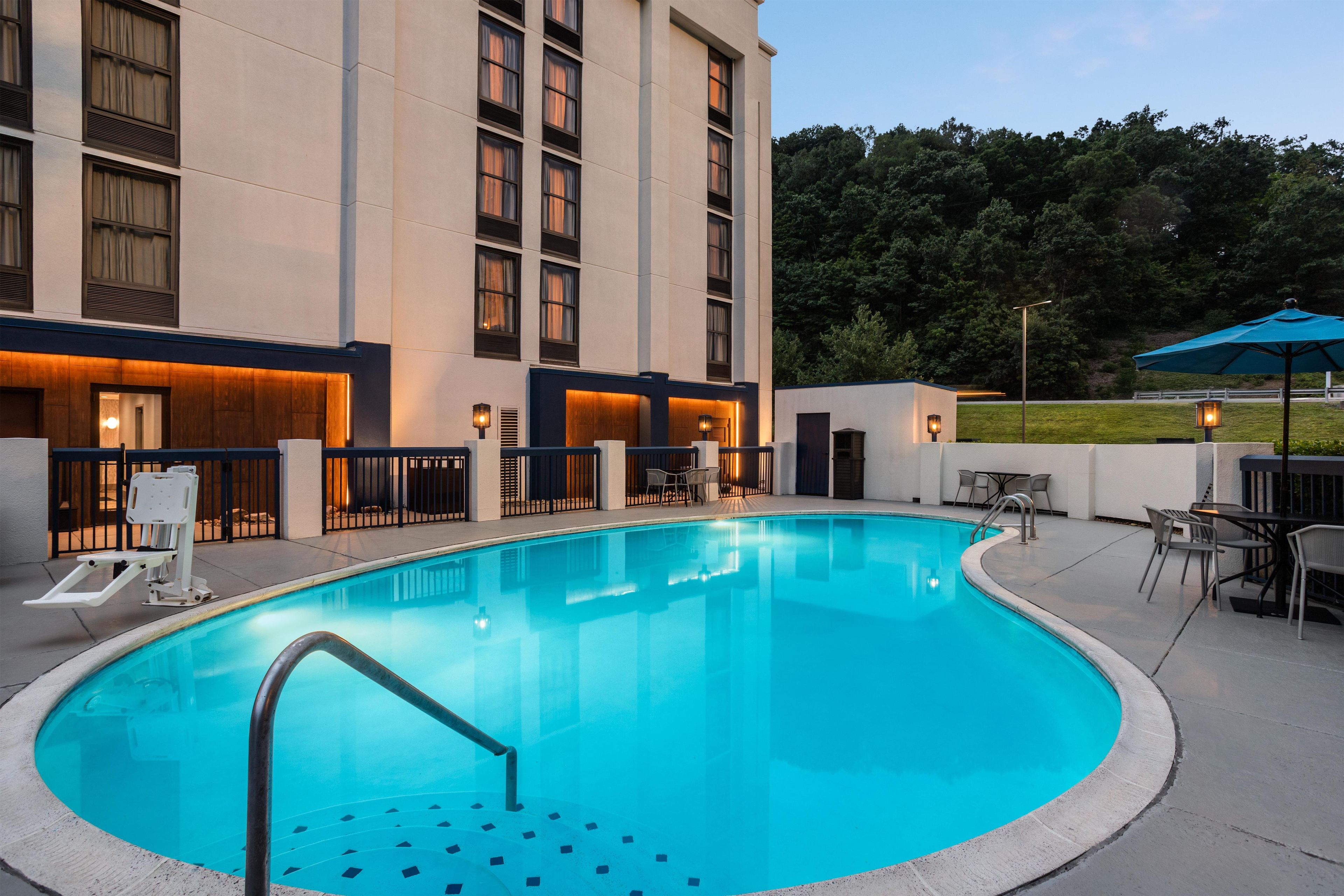 A swimming pool with a metal ladder, surrounded by a building with multiple windows and a covered outdoor seating area.