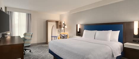A hotel room with a large bed, a desk, a chair, and a television.