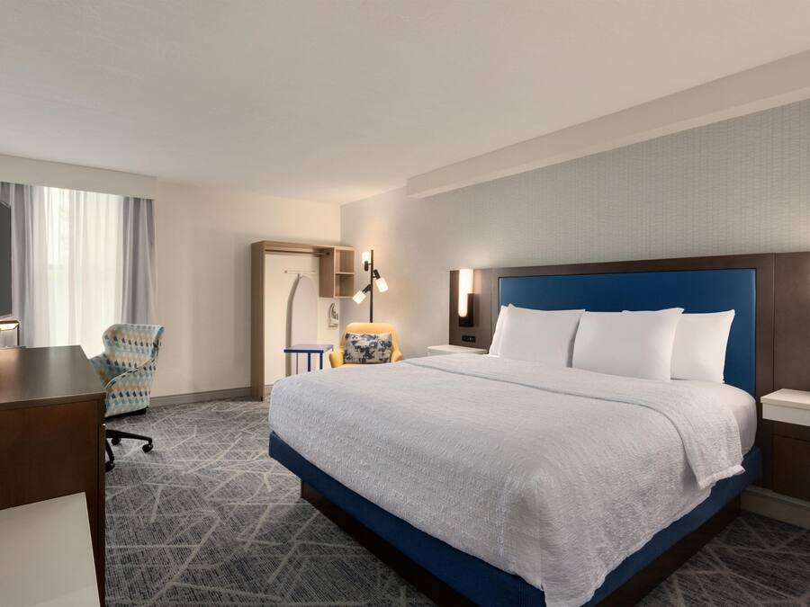 A hotel room with a large bed, a desk, a chair, and a television.