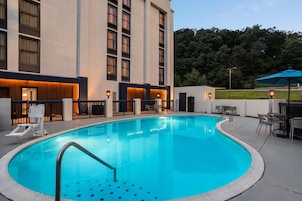 A swimming pool with a metal ladder, surrounded by a building with multiple windows and a covered outdoor seating area.