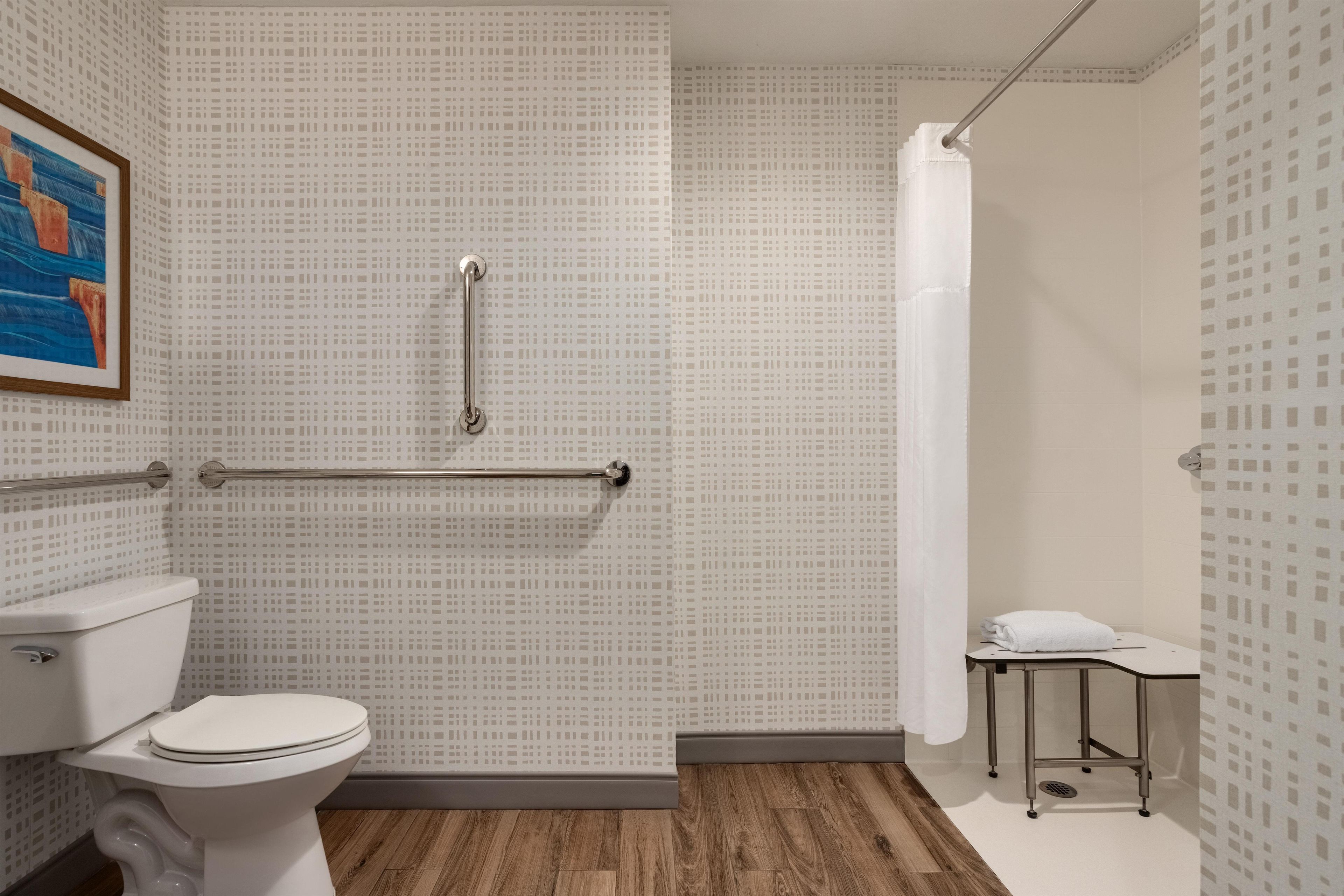 A bathroom with a toilet, grab bars, a shower curtain, and a towel rack.