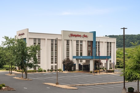 A Hampton Inn hotel with a modern facade, a parking lot, and surrounding greenery.