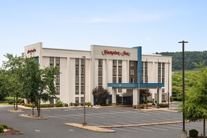 Hotel Hampton Inn com fachada moderna, estacionamento e área verde ao redor.