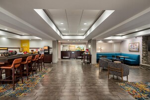 Um hall de hotel com área de bar, assentos e balcão de recepção.