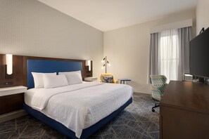 Habitación de hotel con una cama grande, un escritorio, una silla, un televisor y una ventana con cortinas.