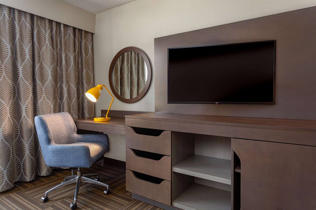 A hotel room with a desk, chair, TV, and a mirror.