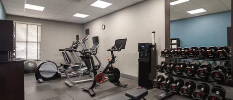 A gym with exercise equipment, a bench, and a rack of dumbbells.