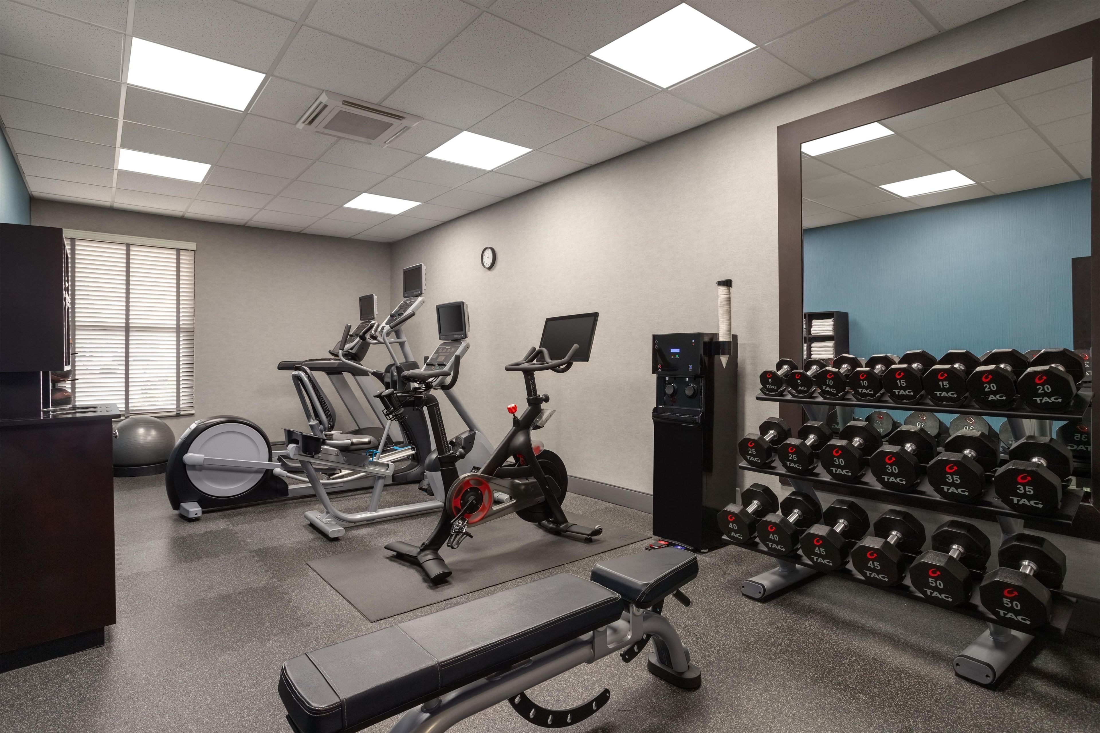 A gym with exercise equipment, a bench, and a rack of dumbbells.