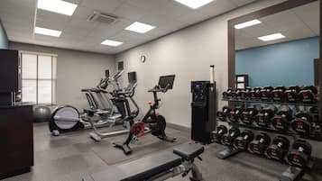 A gym with exercise equipment, a bench, and a rack of dumbbells.