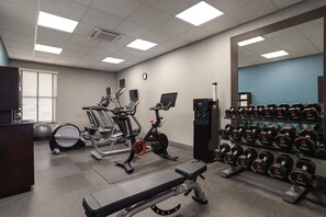 Un gimnasio con equipo de ejercicio, una banca y una estantería con mancuernas.