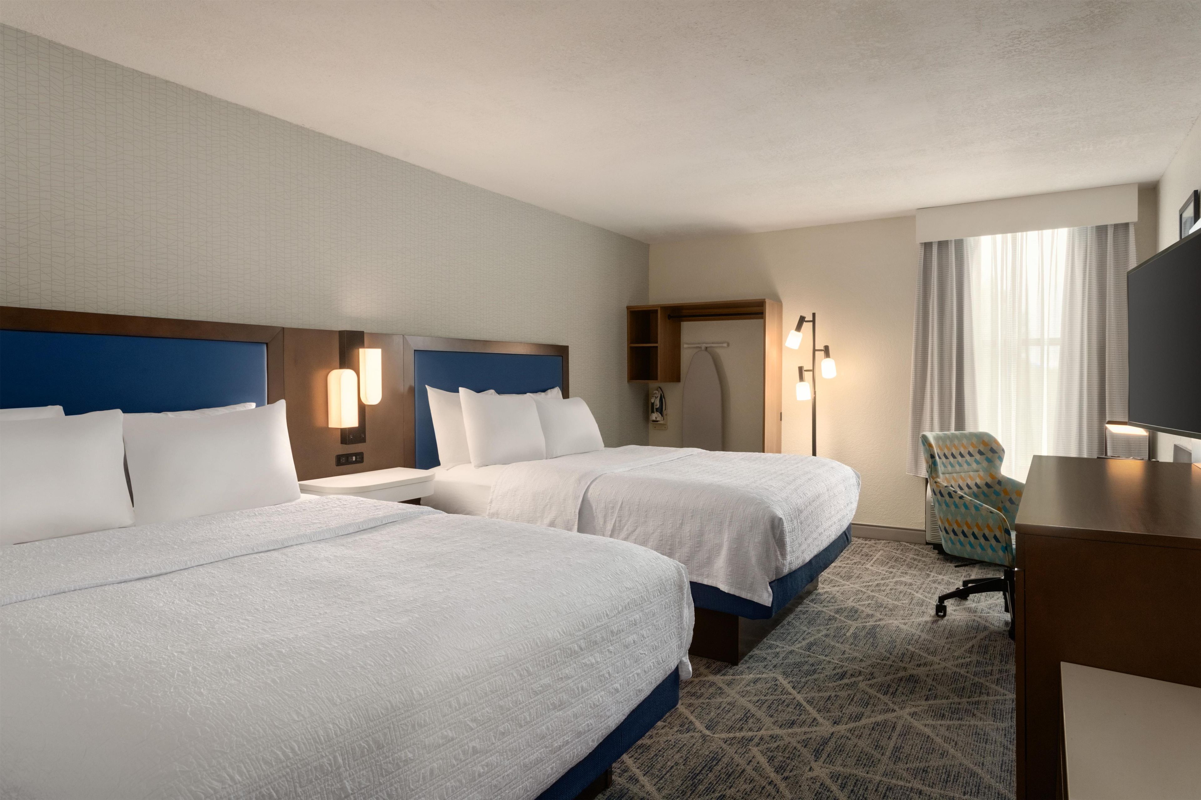 A hotel room with two beds, a desk, a chair, and a walk-in closet.