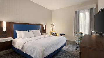 A hotel room with a large bed, a desk, a chair, a television, and a window with curtains.