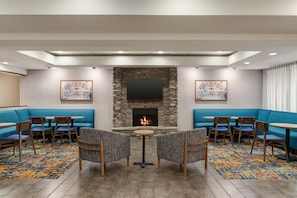 Un hall de hotel con chimenea de piedra, asientos azules y un televisor de pantalla plana.