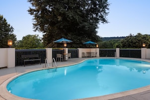 Una piscina con un bordeado, dos sombrillas y una mesa con sillas.
