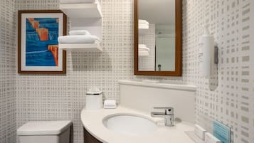Een moderne badkamer met toilet, wastafel en spiegel. Aan de muur hangt een schilderij in een lijst en erboven bevindt zich een handdoekhouder.