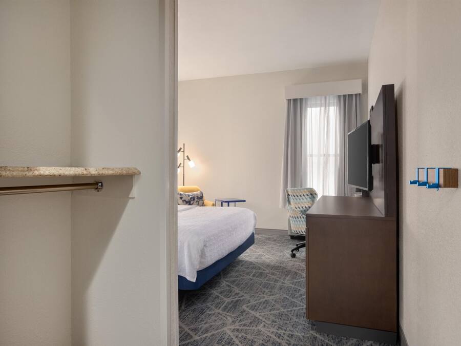 A hotel room with a bed, a desk, a chair, a television, and a minibar.