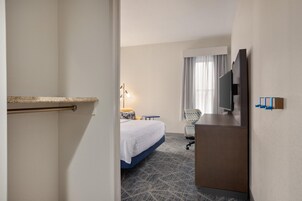 Una habitación de hotel con una cama, un escritorio, una silla, un televisor y un minibar.