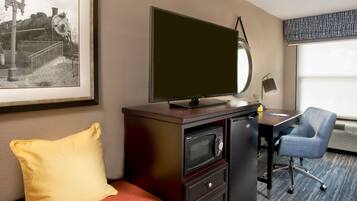 A hotel room with a bed, a desk with a chair, a television, a microwave, and a framed picture on the wall.