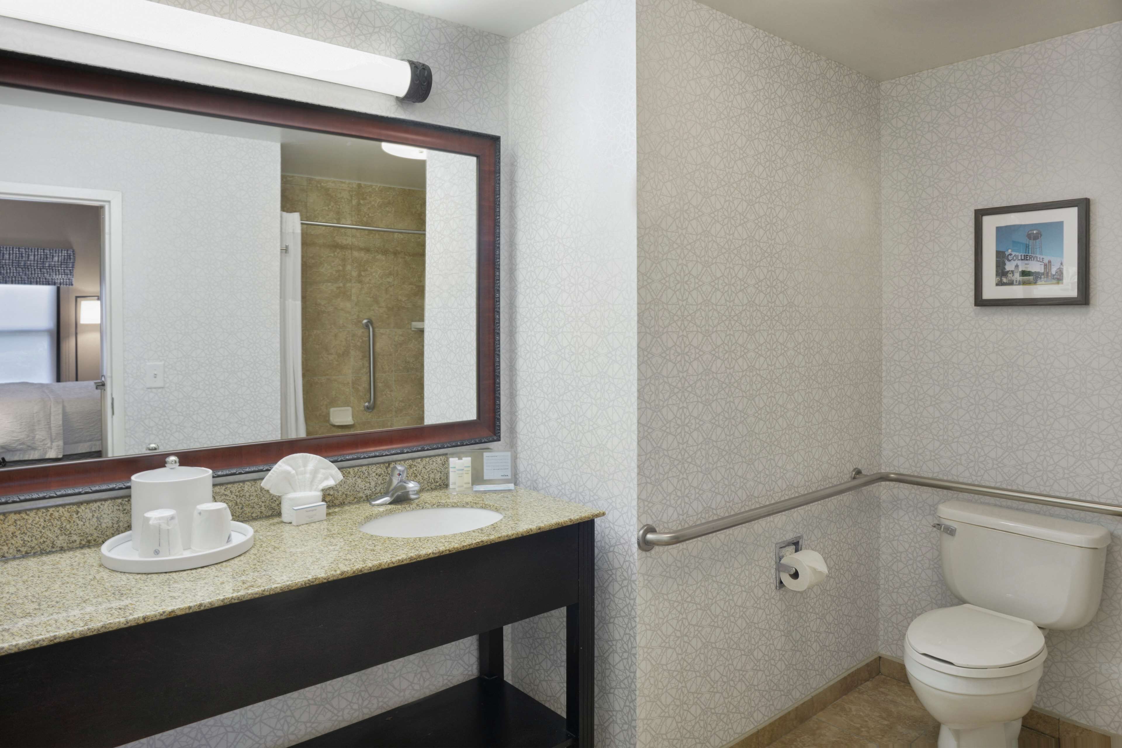 Un baño moderno con encimera de granito, un lavamanos blanco, un espejo grande, inodoro y zona de ducha.