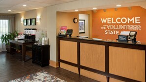 A reception area with a wooden reception desk, a clock, and a sign welcoming volunteers to the state. - Hampton Inn Collierville (Collierville)