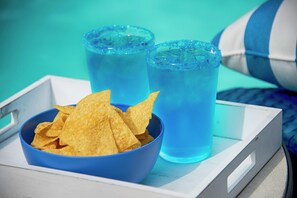 A tray with a blue bowl of chips and two glasses of blue liquid.