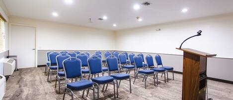 A conference room with rows of blue chairs, a wooden podium, and a carpeted floor.