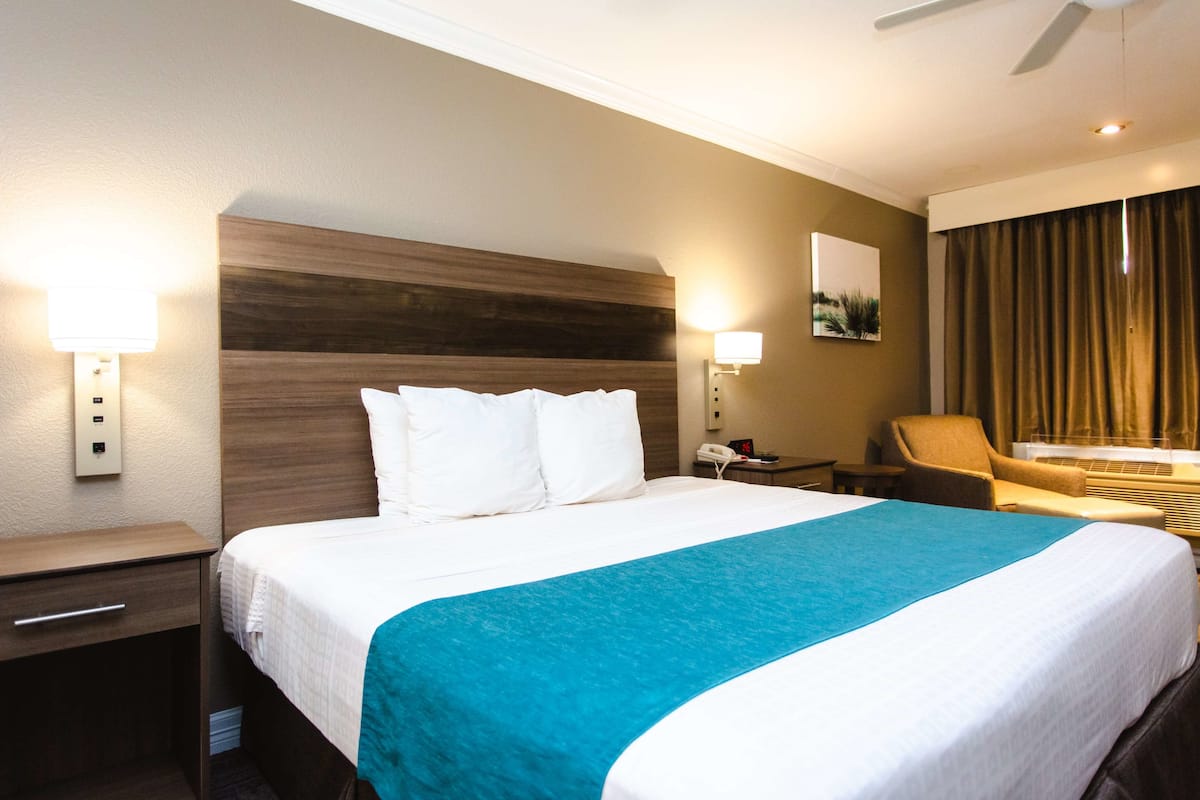 A hotel room with a large bed, a nightstand, a desk, a chair, and a wall-mounted telephone.
