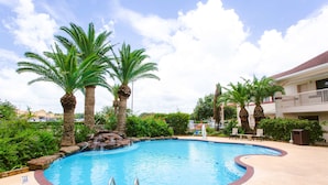 A swimming pool with palm trees, a waterfall feature, and a lounge area with chairs. - Best Western Pearland Inn (Pearland)