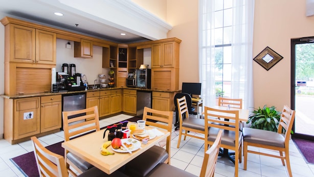 A modern kitchen with wooden cabinets, a dining area with a table and chairs, and a large window providing natural light. - Best Western Pearland Inn (Pearland)