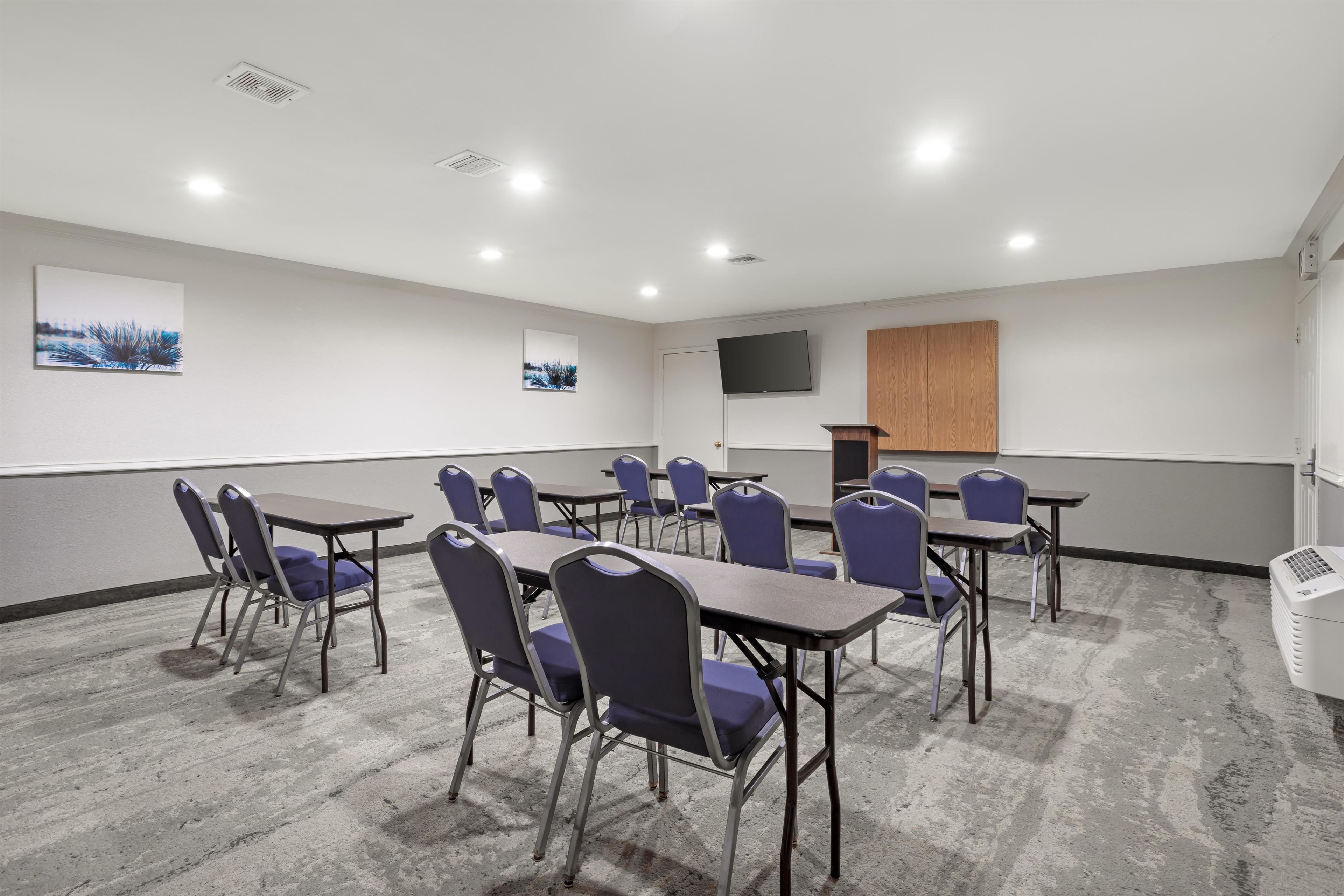 Un salón de conferencias con mesas y sillas, un televisor de pantalla plana y obras de arte en las paredes.