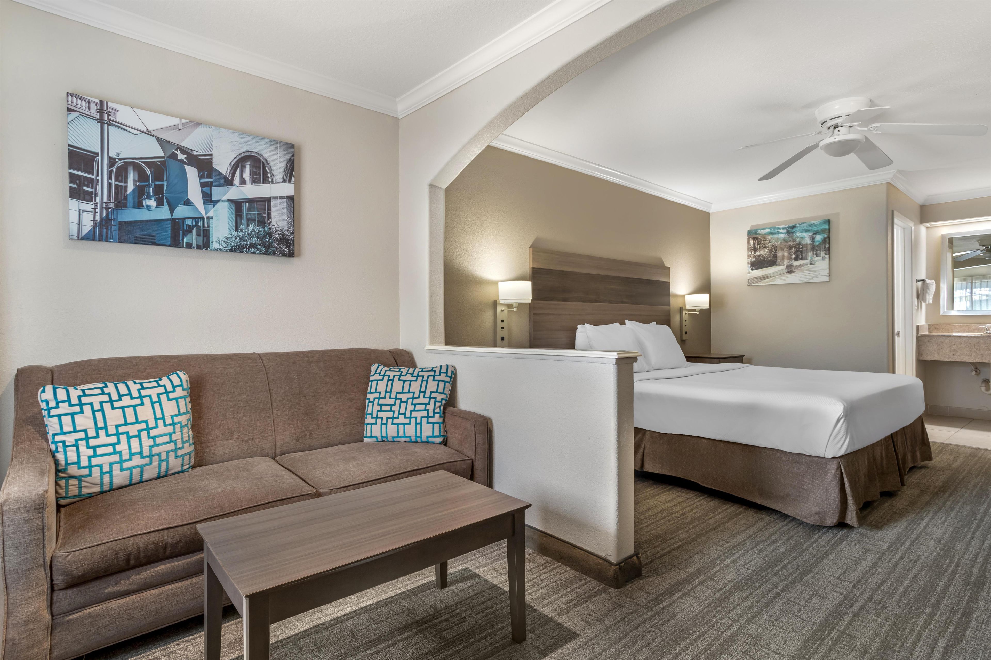 A hotel room with a sofa, a bed, a table, and a ceiling fan.