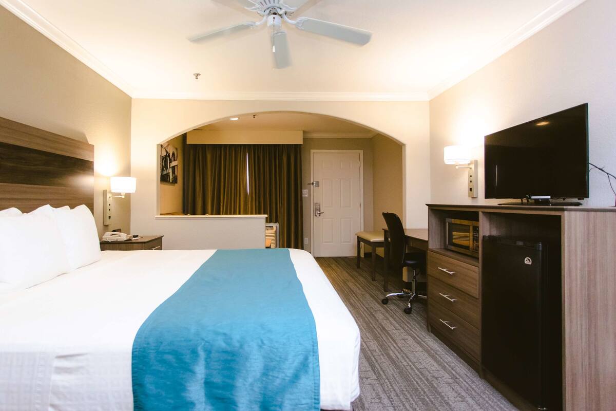 A hotel room with a large bed, a desk, a television, and a ceiling fan.