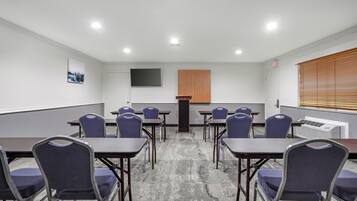 A conference room with tables and chairs, a flat-screen TV, a wooden panel, and a window with blinds.