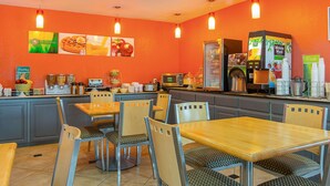 Un restaurante con paredes anaranjadas, mesas y sillas de madera. Se observan vitrinas con alimentos y una máquina de café.