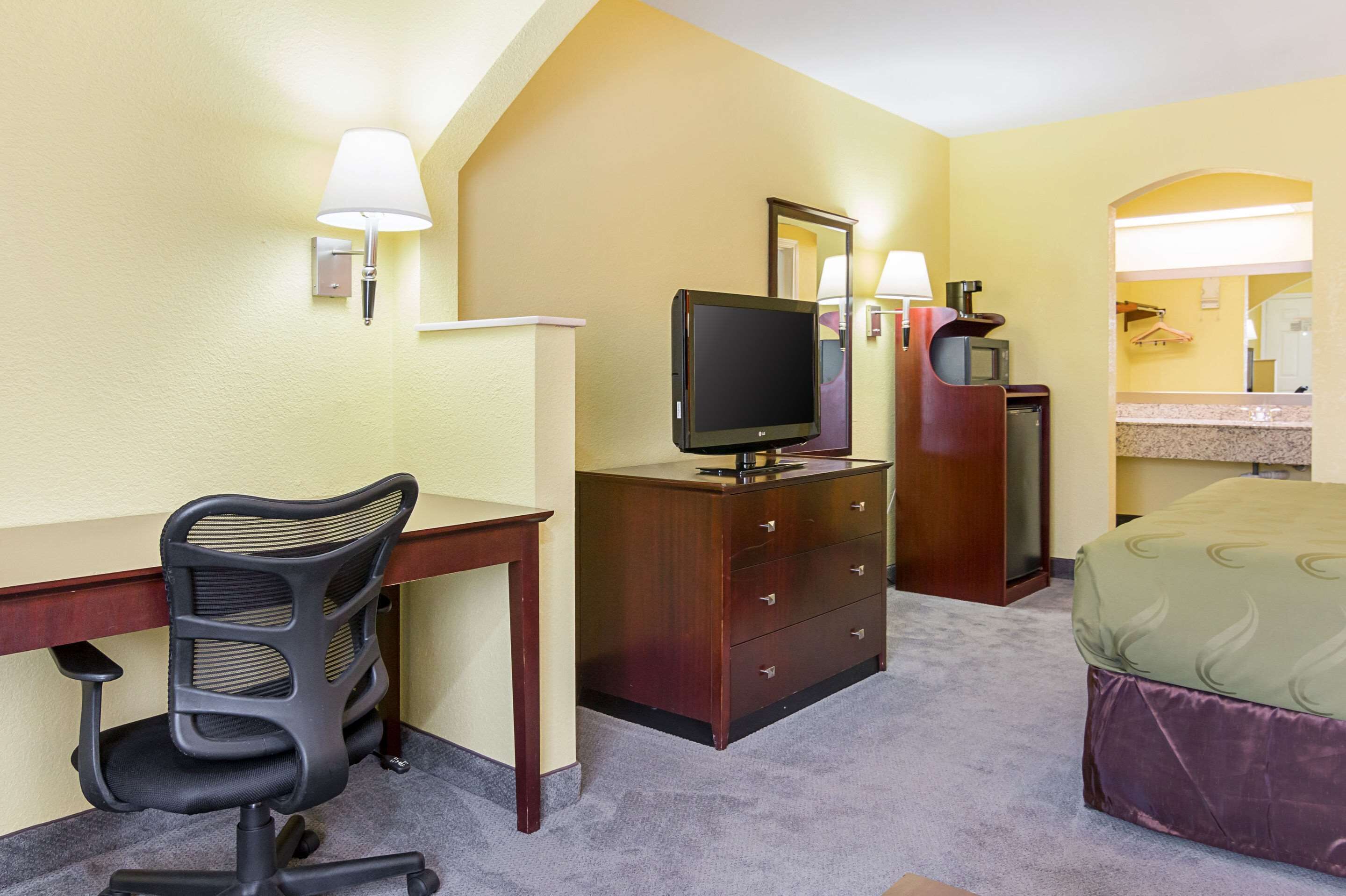 Ein Hotelzimmer mit Schreibtisch, Stuhl, Fernseher, Kommode und Bett.