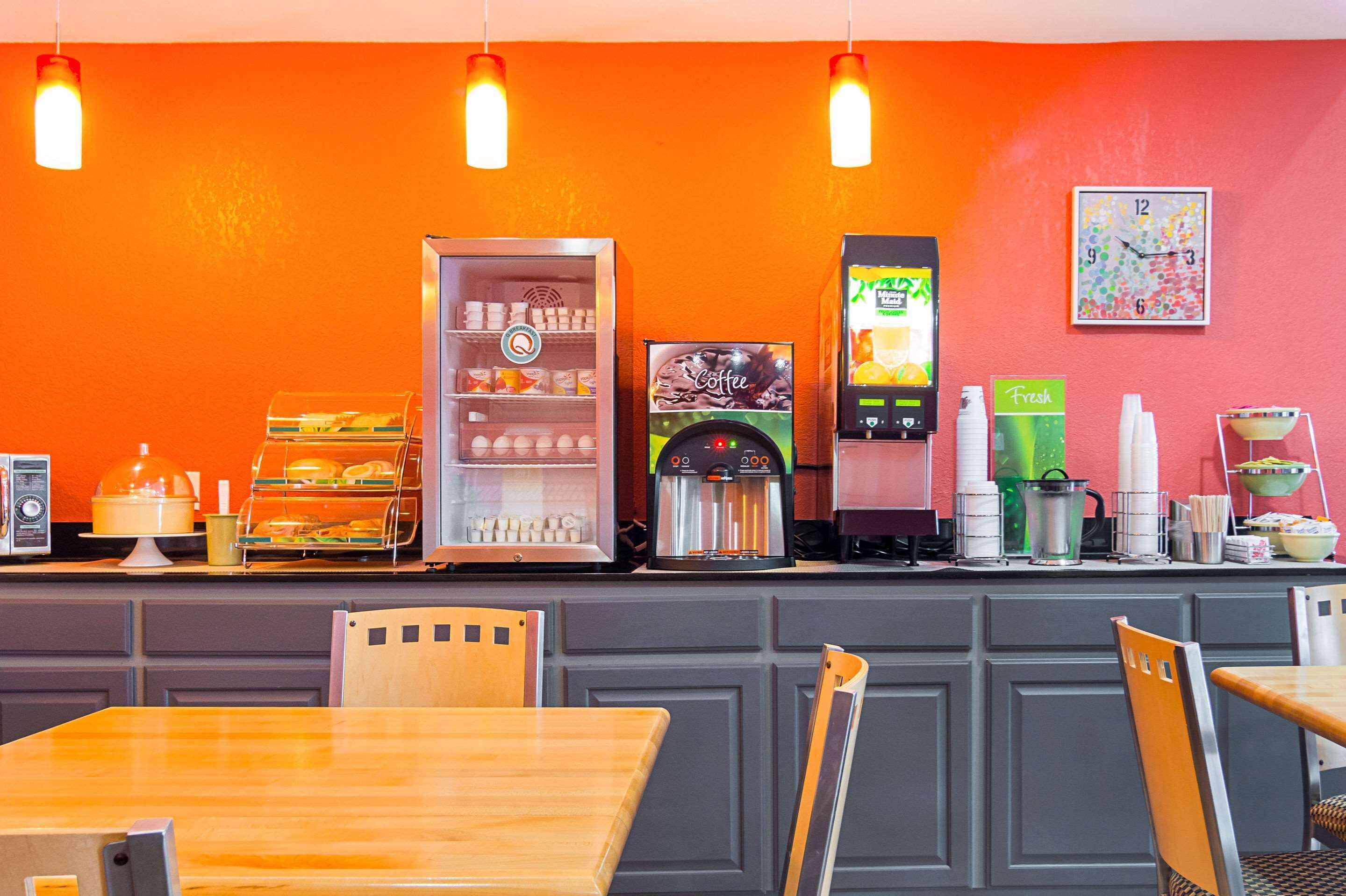 Una cafetería con un mostrador que exhibe varias máquinas de café, un refrigerador con bebidas y un reloj en la pared.