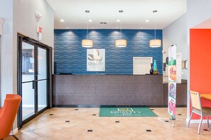 Et hotelreceptionsområde med en blå bølget væg, en receptionsdisk og en grøn måtte på gulvet.