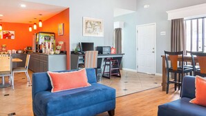 Una sala moderna con un sofá azul, un comedor con mesa y sillas, una zona de cocina con electrodomésticos, y una puerta con la etiqueta 'Bedroom'.