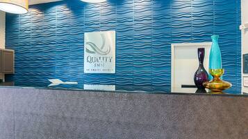 A reception area with a blue wavy wall, a sign for Quality Inn, and a reception desk with decorative vases.