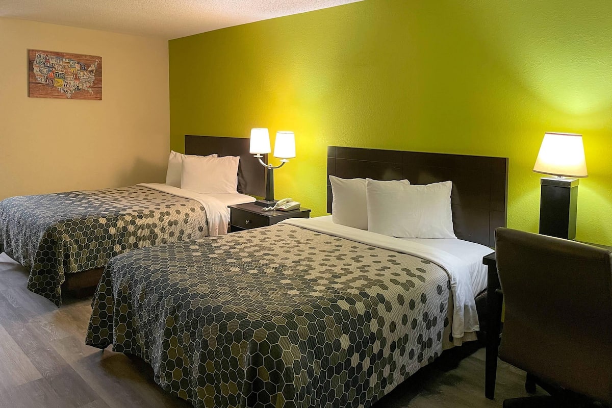 A hotel room with two beds, each with a patterned bedspread, a nightstand with a lamp, and a wall map.