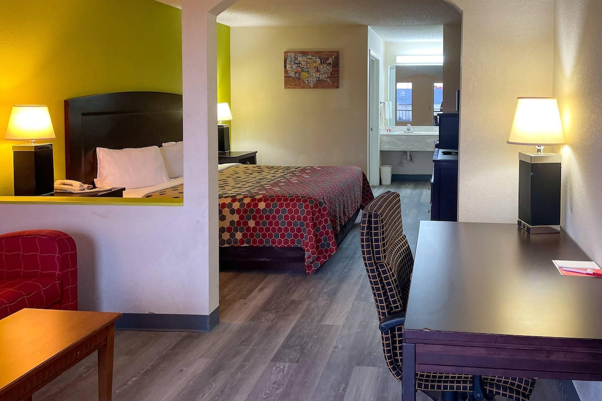 A hotel room with a bed, a desk, a chair, a table, and a bathroom visible through an open door.