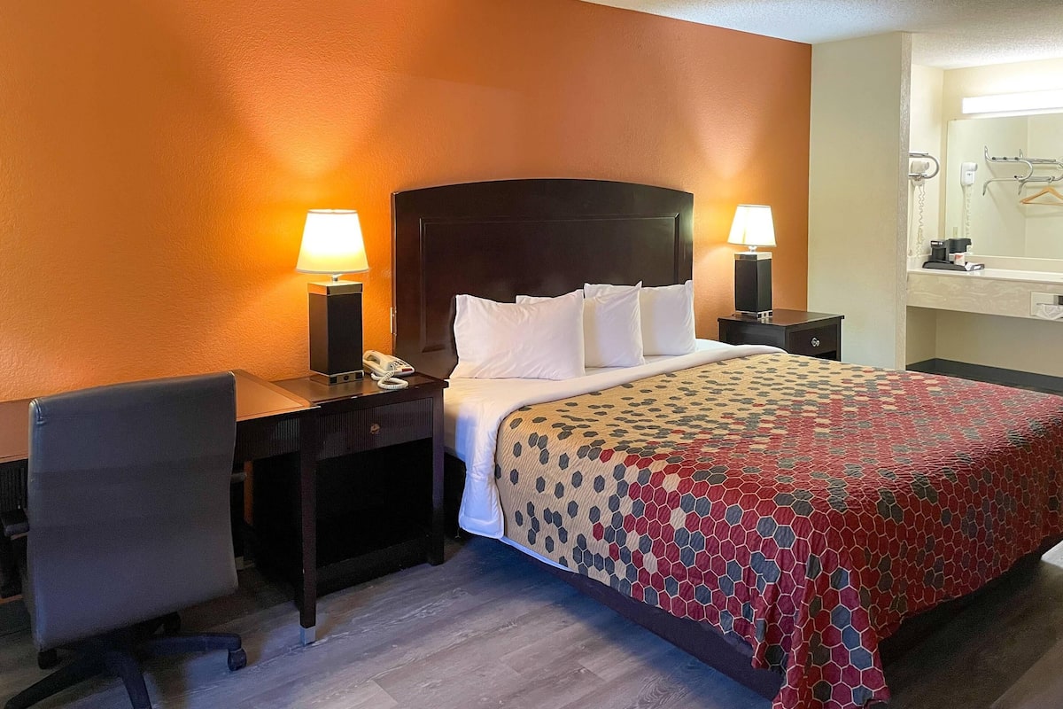 A hotel room with a bed, two bedside lamps, a desk with a chair, and a mirror above the bed.