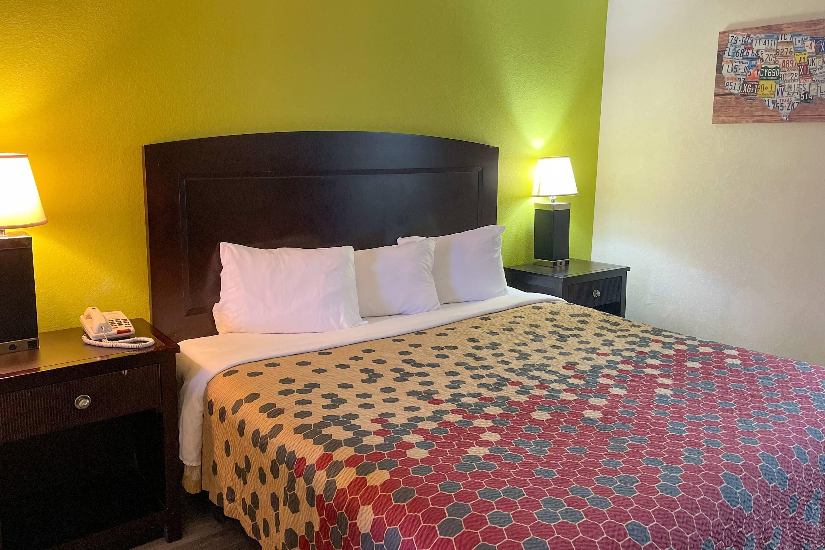 A hotel room with a bed, a nightstand with a lamp, and a wall-mounted telephone.