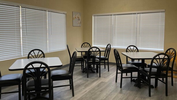 A dining area with tables and chairs, large windows with blinds, and a wooden floor. - Econo Lodge Inn & Suites Sweetwater I-20 (Sweetwater)