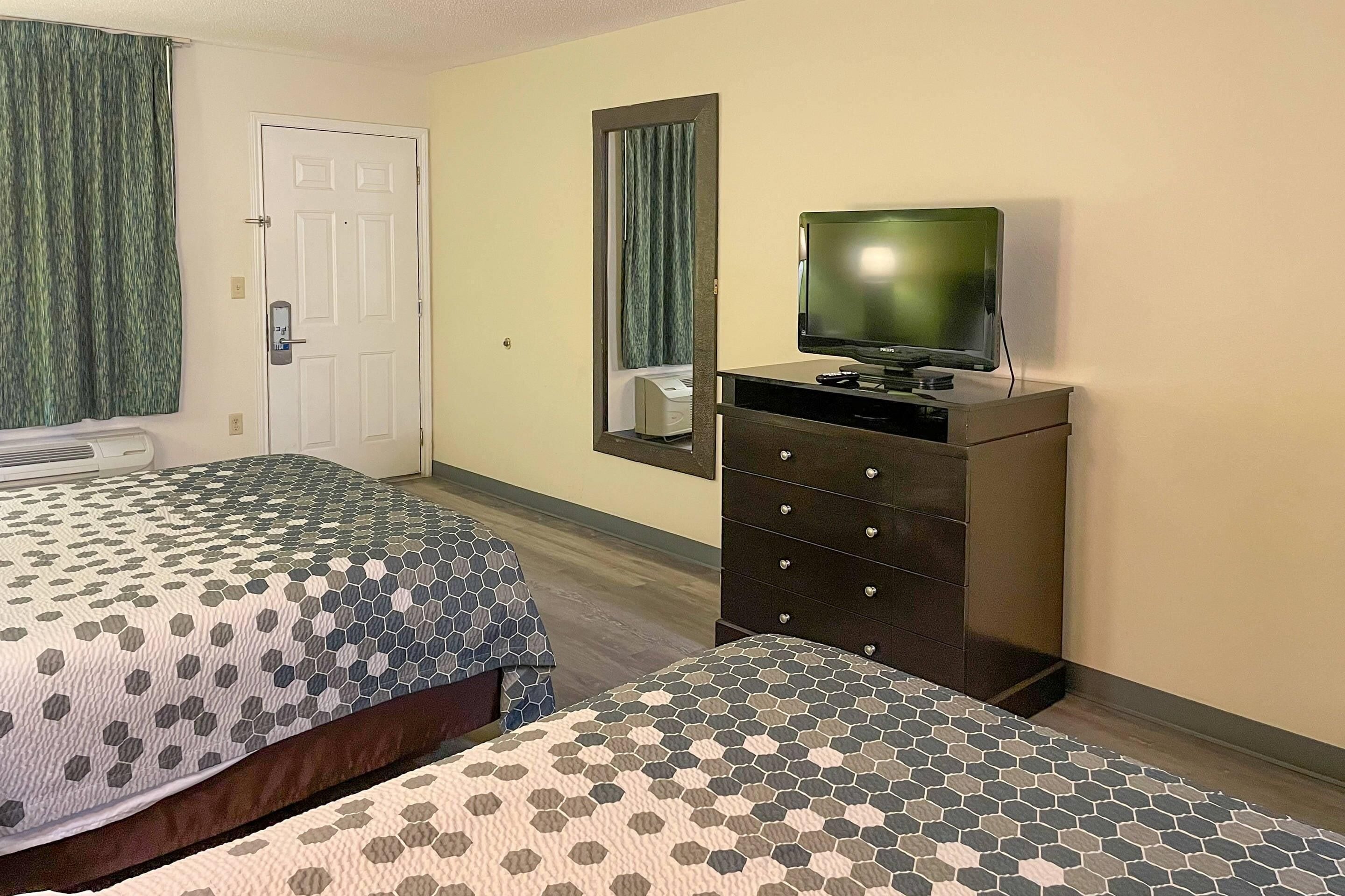 A hotel room with two beds, a dresser, a television, and a door with a mirror.