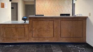 A reception desk with a wooden finish, a digital check-in kiosk, and a patterned wall behind it. - Econo Lodge Inn & Suites Sweetwater I-20 (Sweetwater)