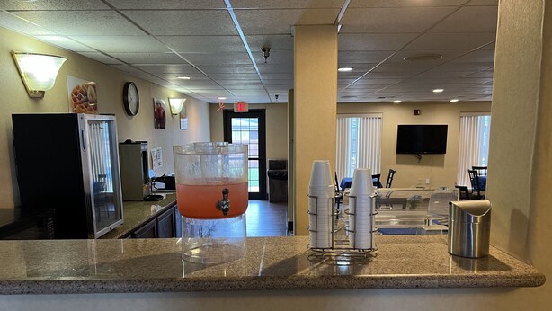 A kitchen area with a beverage dispenser, a refrigerator, and a dining area with tables and chairs. - Americas Best Value Inn Pharr (Pharr)